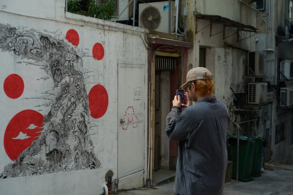 Persona fotografiando un mural urbano colorido con su smartphone en la calle