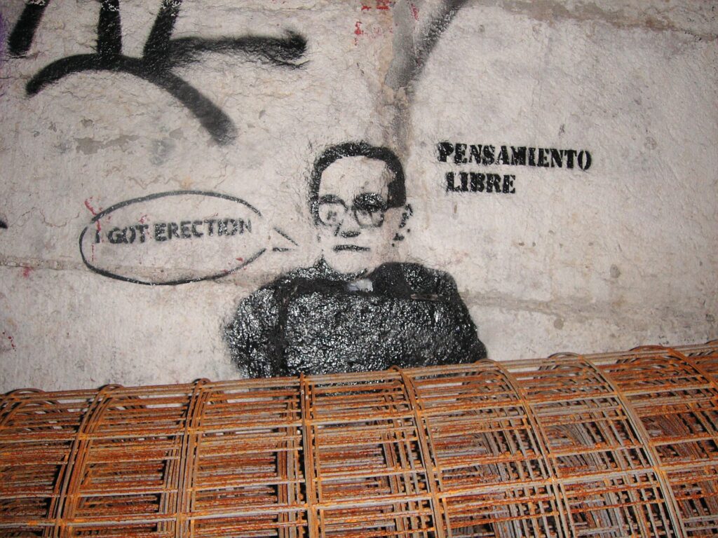 Rodillo cargado de pintura apoyado en un cubo delante de una pared a medio pintar