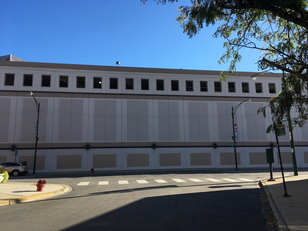 Fachada ciega de un edificio alto vista desde una calle estrecha con coches aparcados