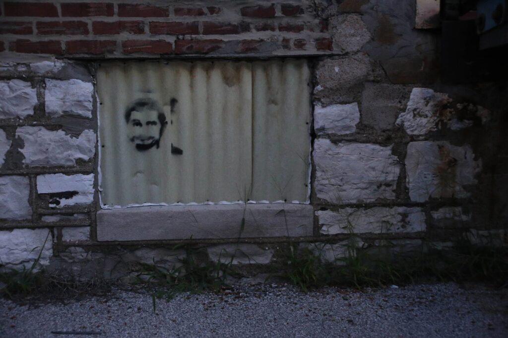 Pequeña figura pintada junto a una puerta metálica de servicio a la altura de la rodilla