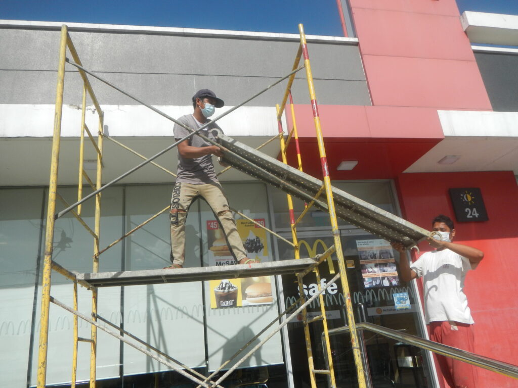 Dos pintores trabajando sobre un andamio en la fachada lateral de un bloque