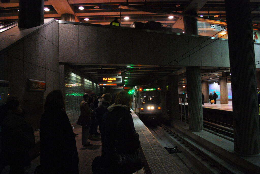 Andén de metro con paneles de información y pocos viajeros esperando